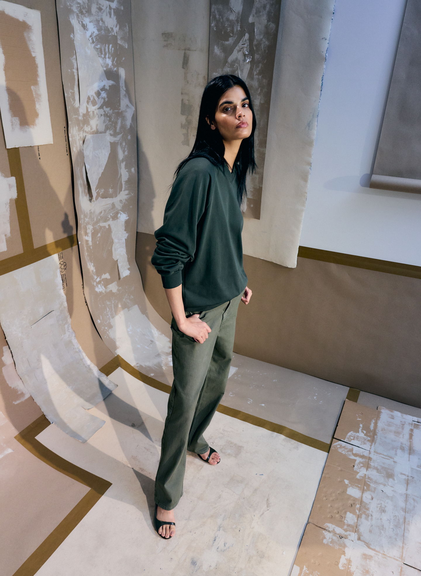 Woman in a green sweater and pants standing against a textured background.