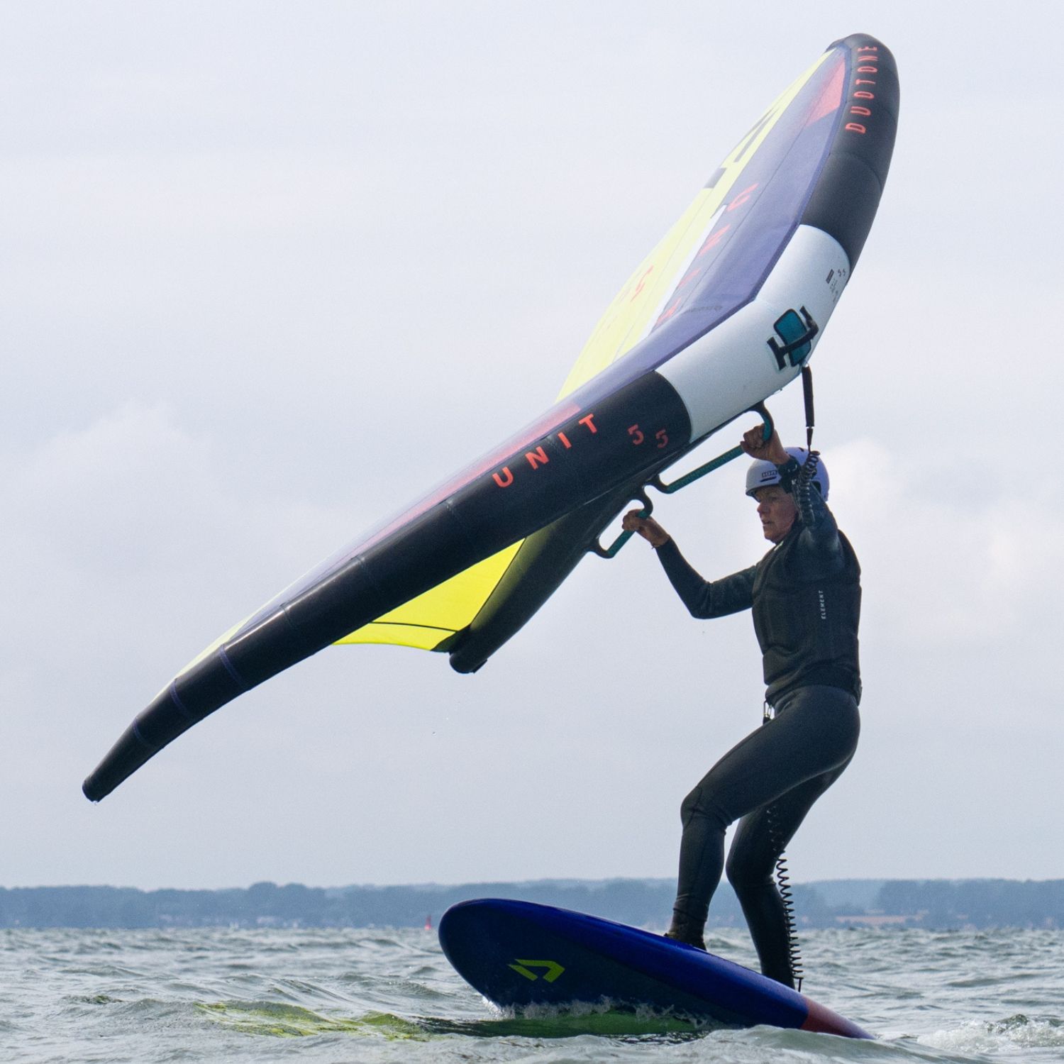 Person surfing on a board while holding a large wing above them.