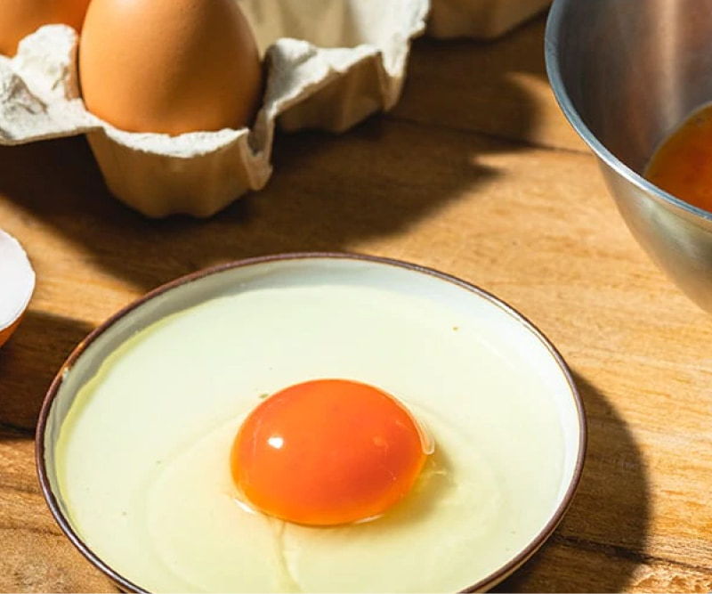 A cracked egg with a bright yolk on a wooden surface.