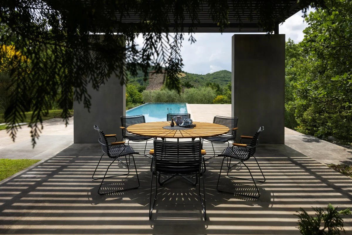 Contemporary pergola-covered outdoor dining area with striped shadows, modern dining furniture, and scenic landscape views designed for comfortable alfresco entertaining.