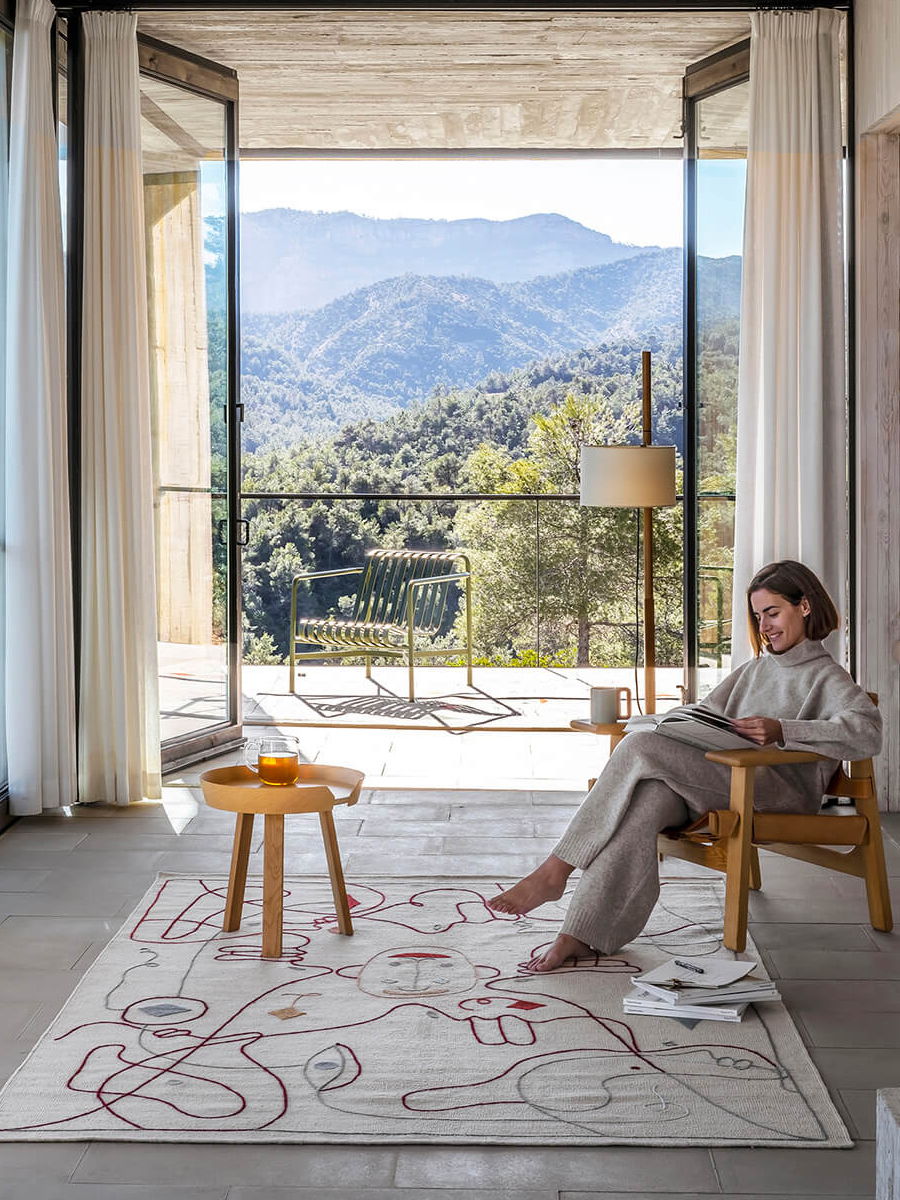 Woman sitting in a chair, overlooking mountains through large glass doors.