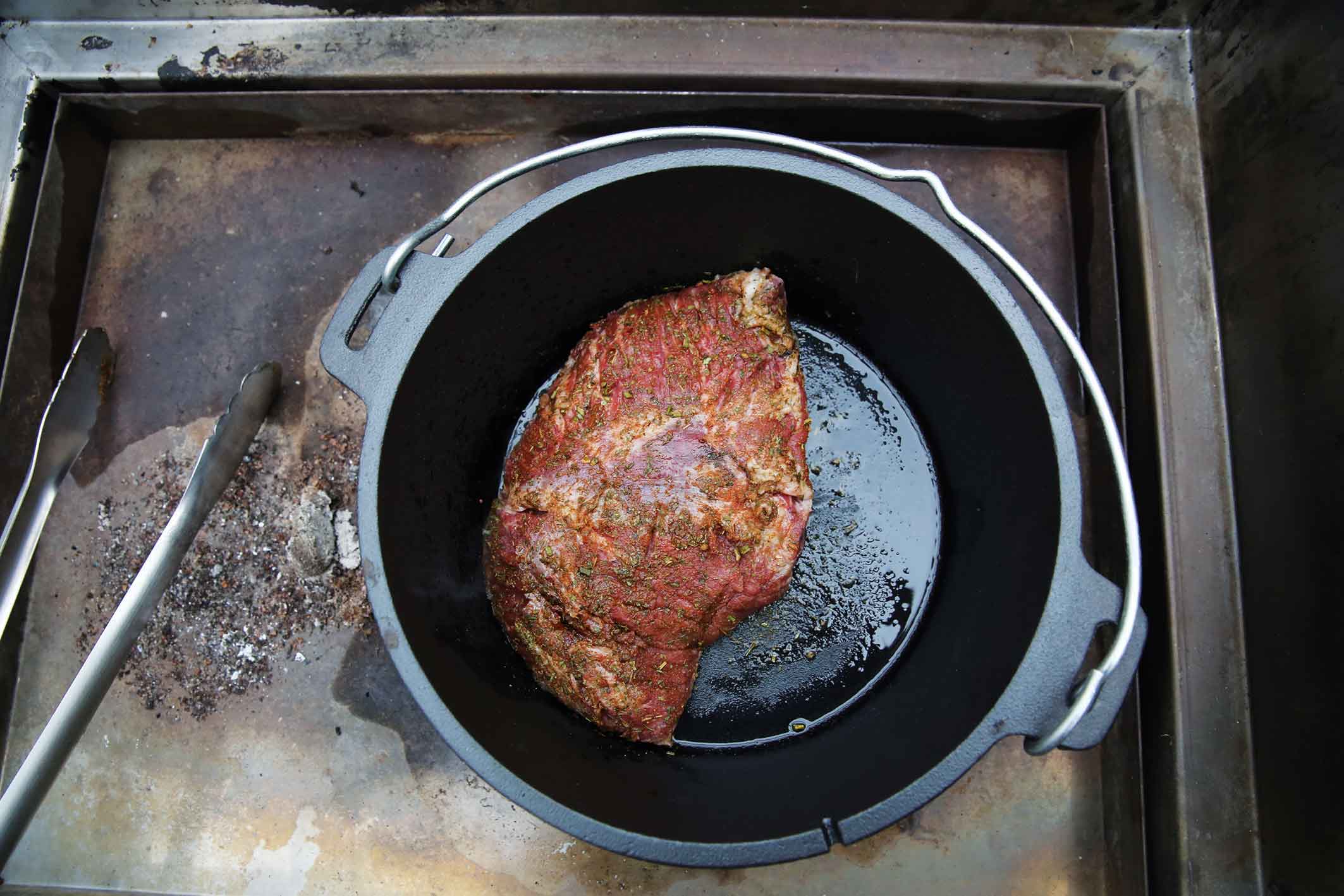 A seasoned roast in a black pot on a cooking surface.