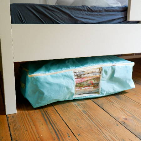 A quilt storage bag wit quilts stored under a bed