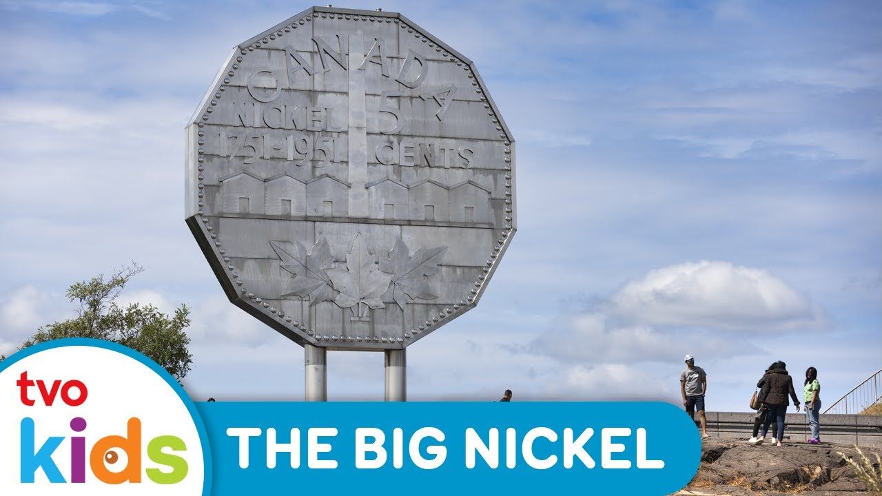 A large nickel monument with people walking nearby under a blue sky.