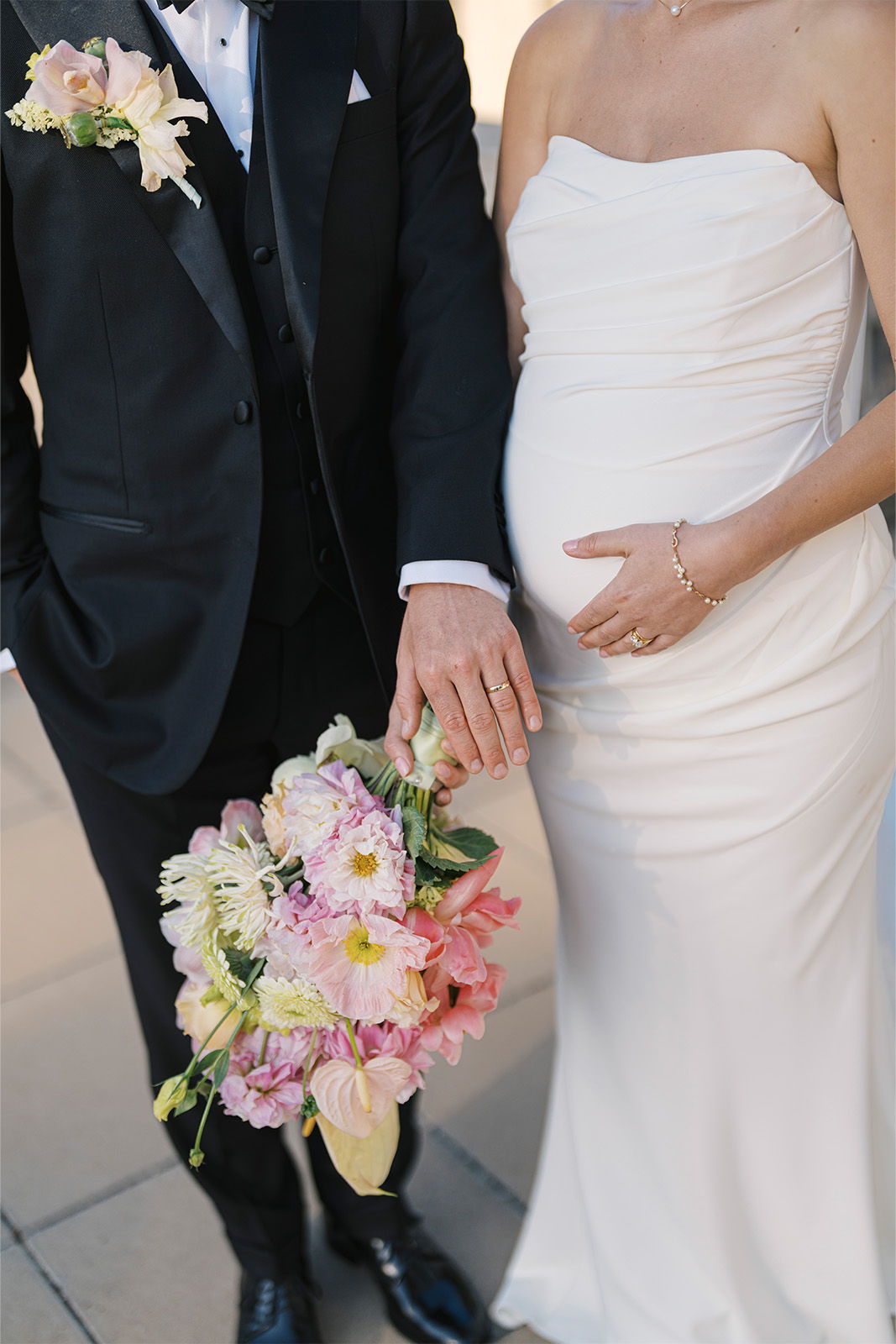 Couple in formal wear, holding a bouquet, showcasing a pregnant belly.