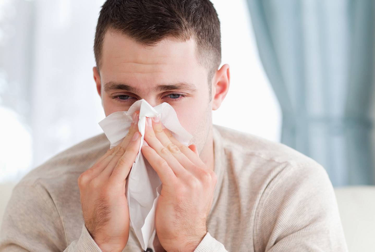 Muž smrká. Plný nos je běžným příznakem alergie na roztoče, která se obvykle projevuje v interiérech.