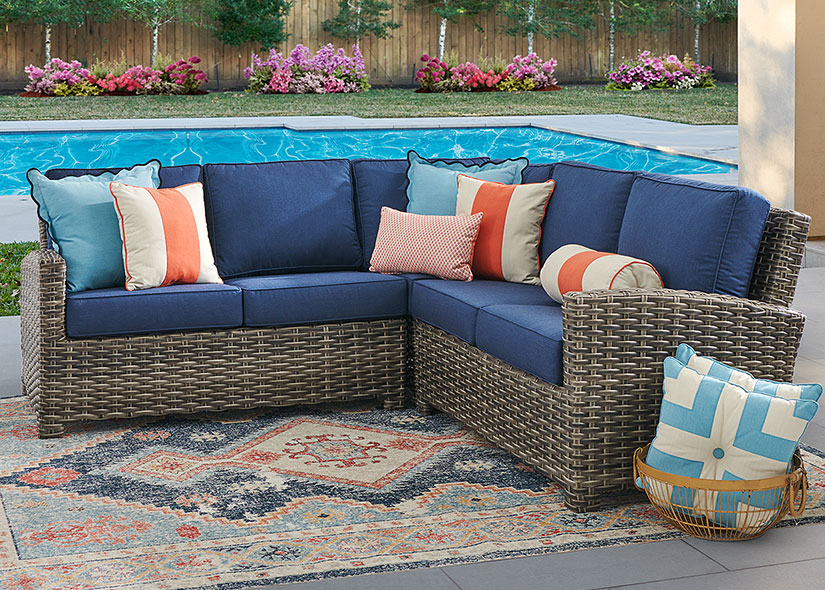 Outdoor sectional sofa with colorful pillows by a swimming pool.