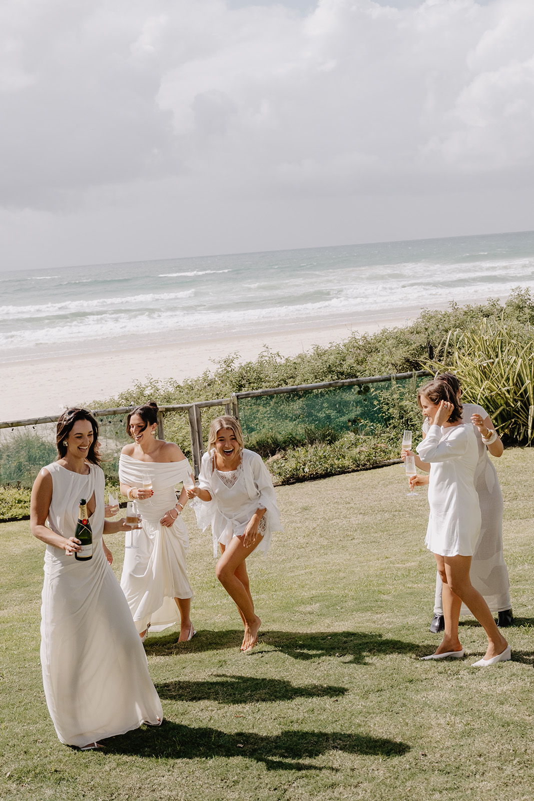 Group of women in white dresses celebrating near the beach.