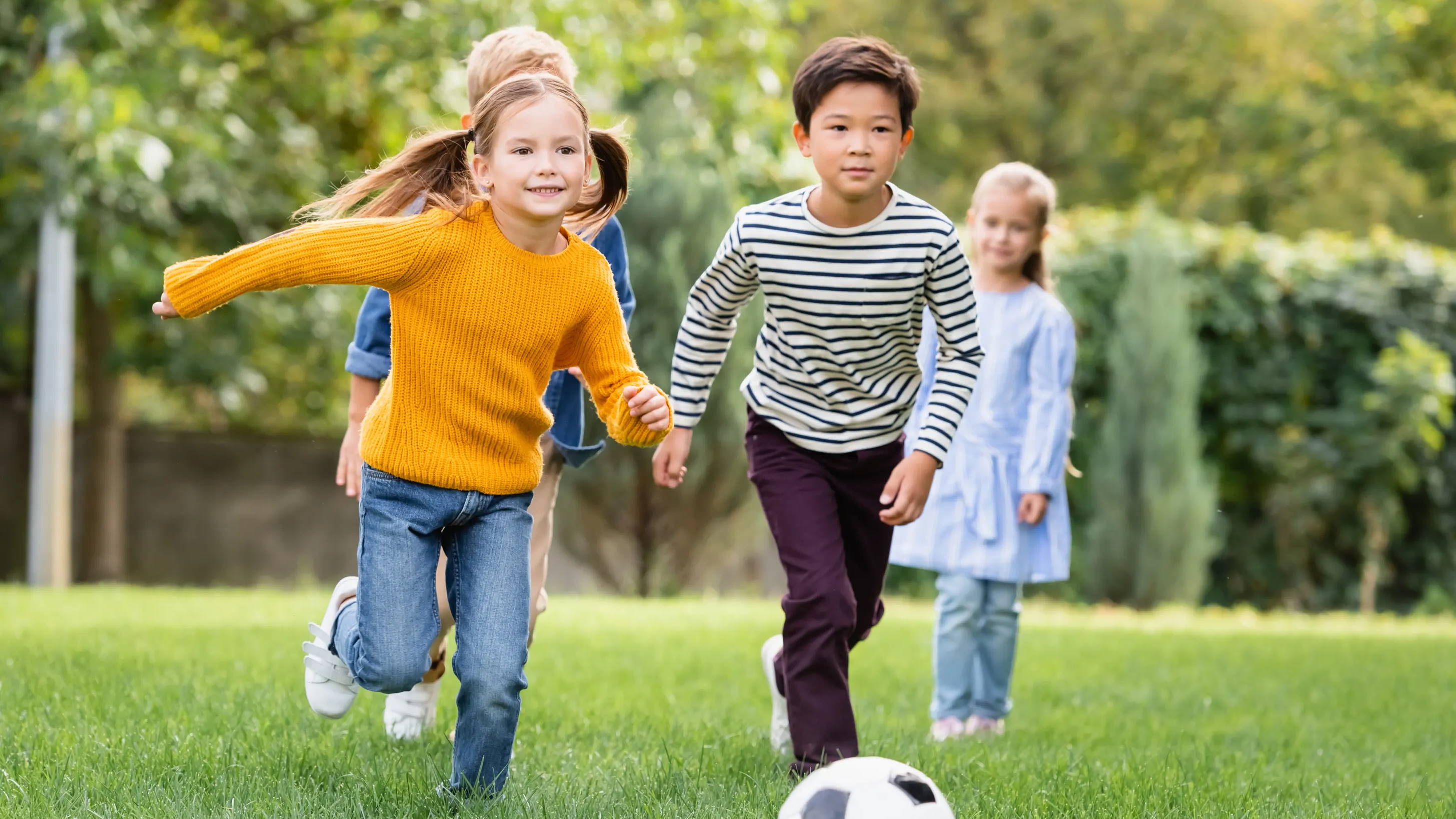 Children running through grass with a soccer ball