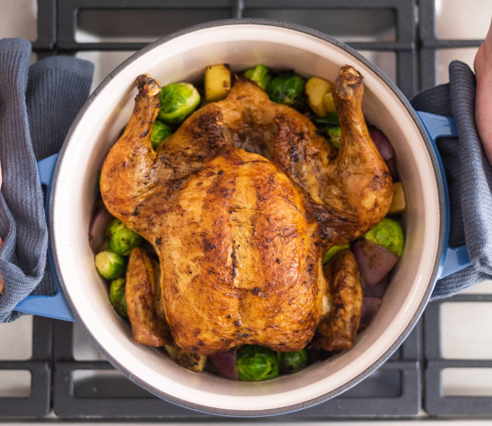 Uncovered Blue Misen Dutch Oven seen from above on a stovetop. A roast chicken with vegetables is visible inside.