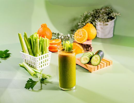 Fresh green smoothie with celery, cucumber, and citrus fruits on a table.