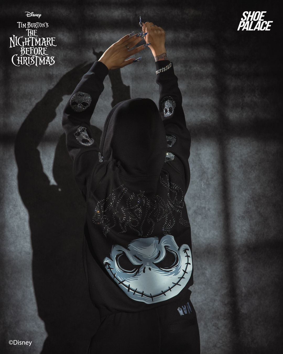 Person wearing a hoodie with a Jack Skellington design, arms raised.