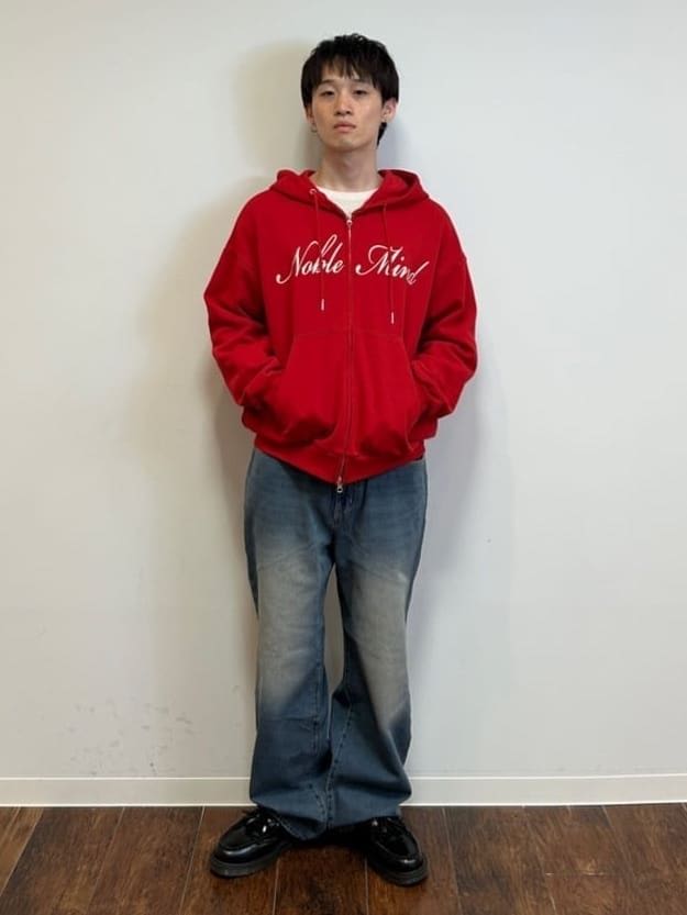 Person standing against a wall, wearing a red hoodie and baggy jeans.