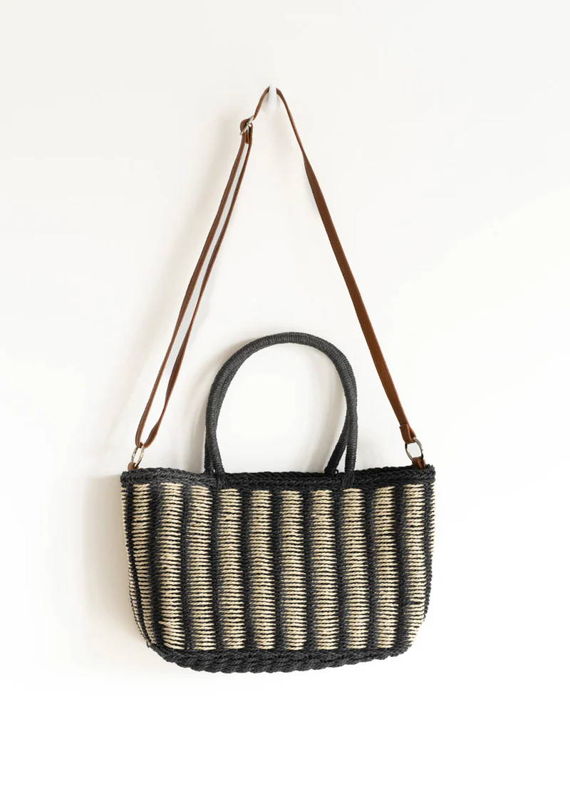 A black and white striped wicker basket with a leather shoulder strap