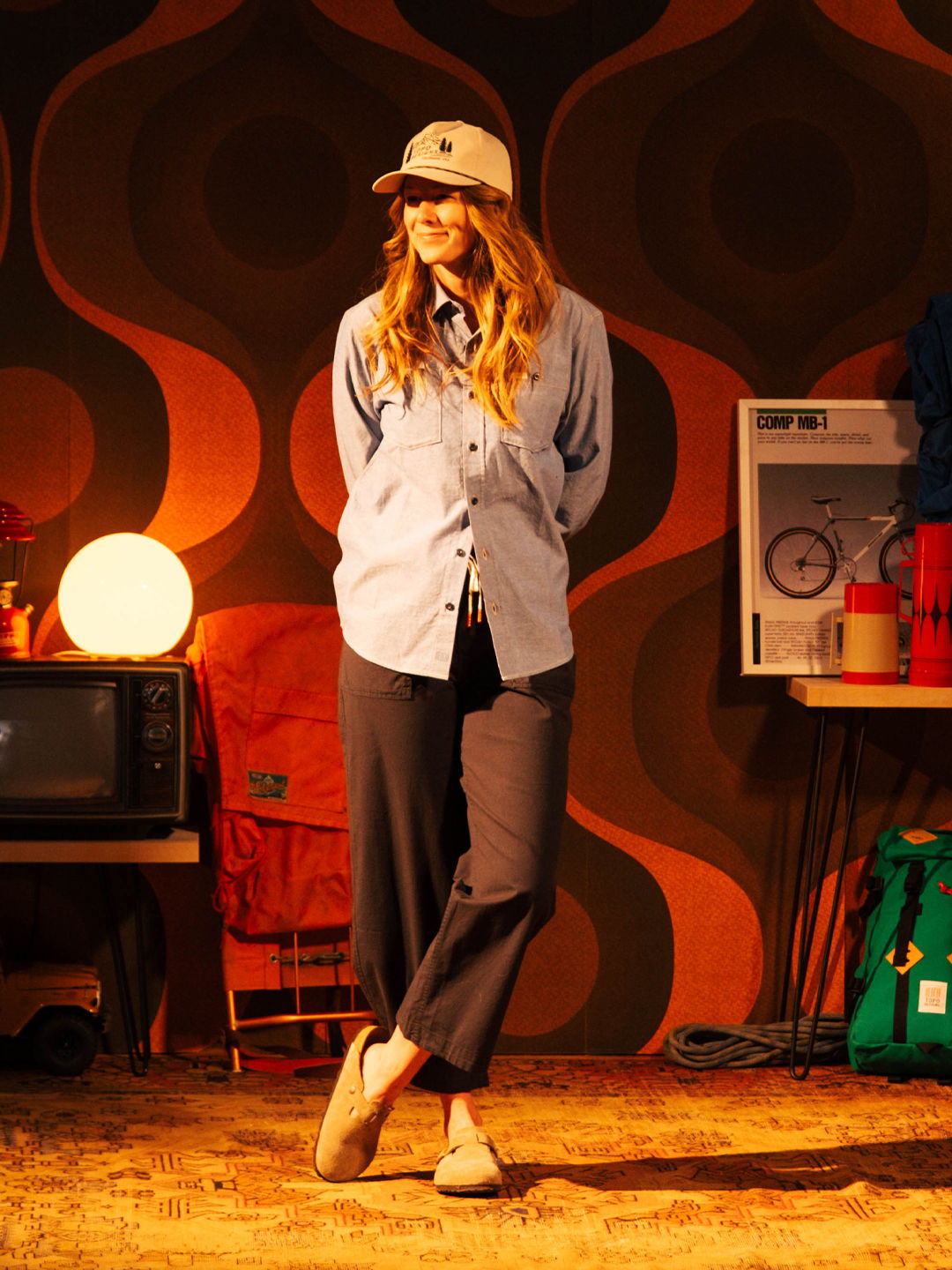 Person wearing a blue shirt and cap, standing in a retro-themed room.