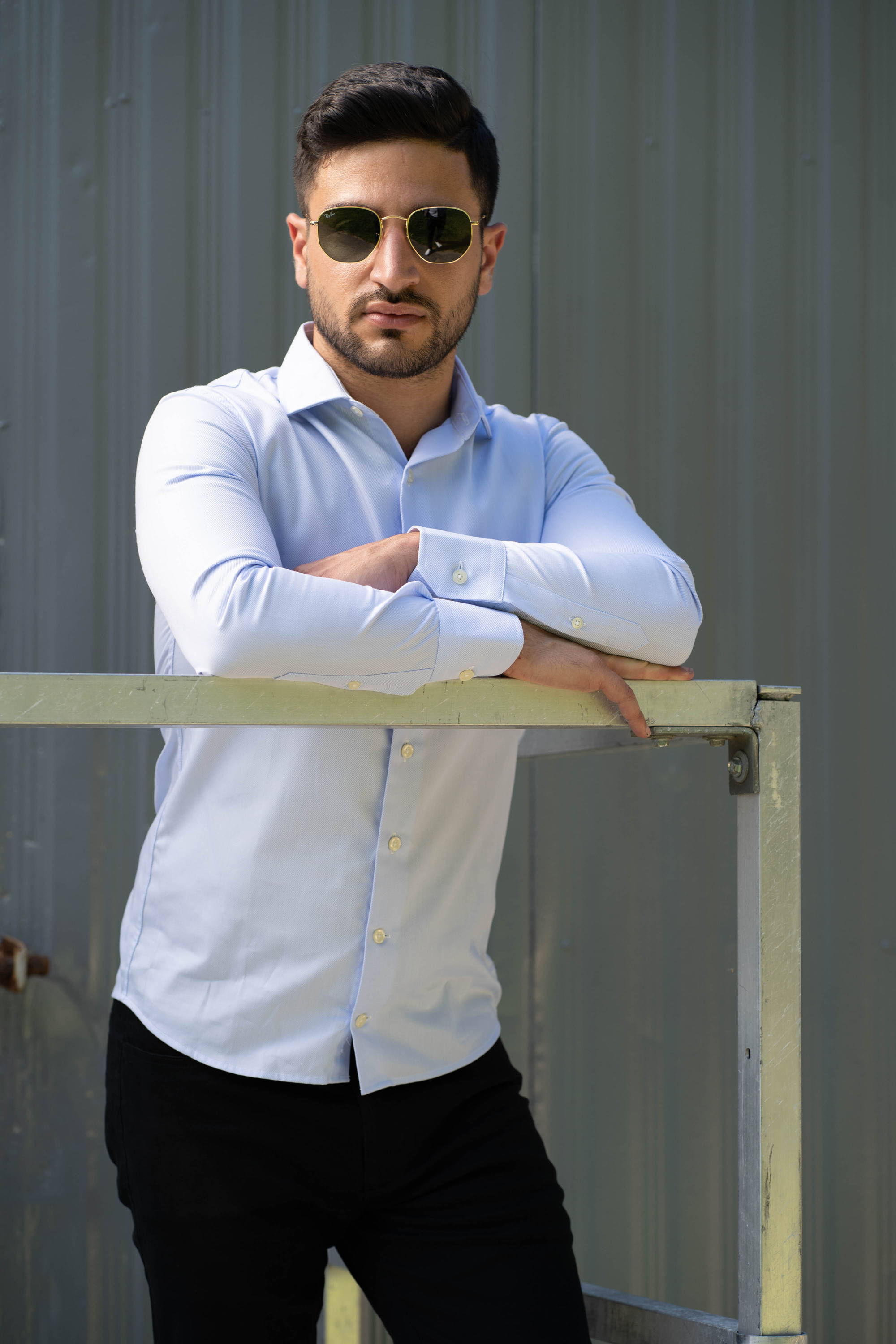 Man standing wearing sunglasses, a light blue dress button down shirt, and black chinos from under510.com