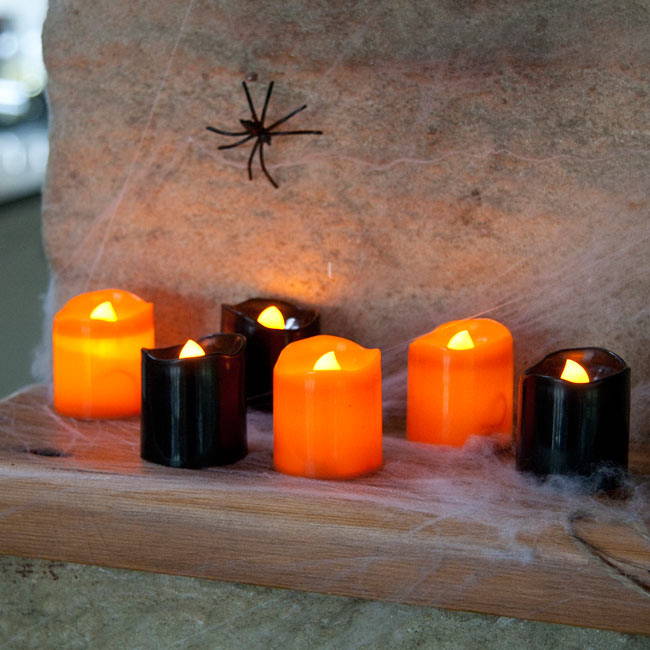 6 black and orange LED candles on a shelf with a spider and cobwebs around them.