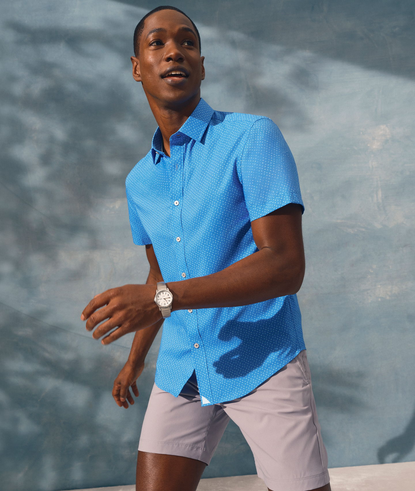 Man in blue shirt and shorts walking against a blue background.
