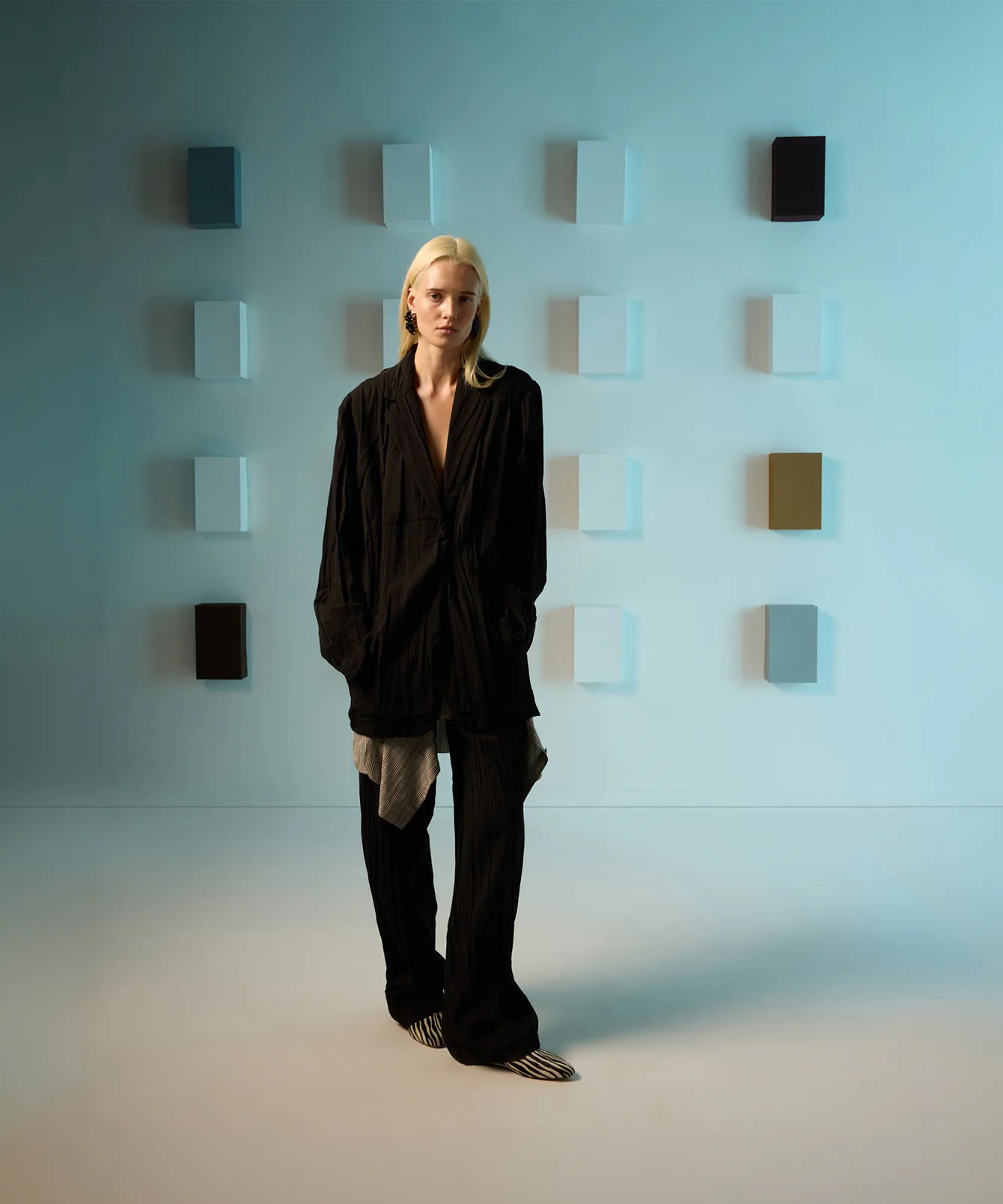 A model in a black outfit stands before a colorful wall display.