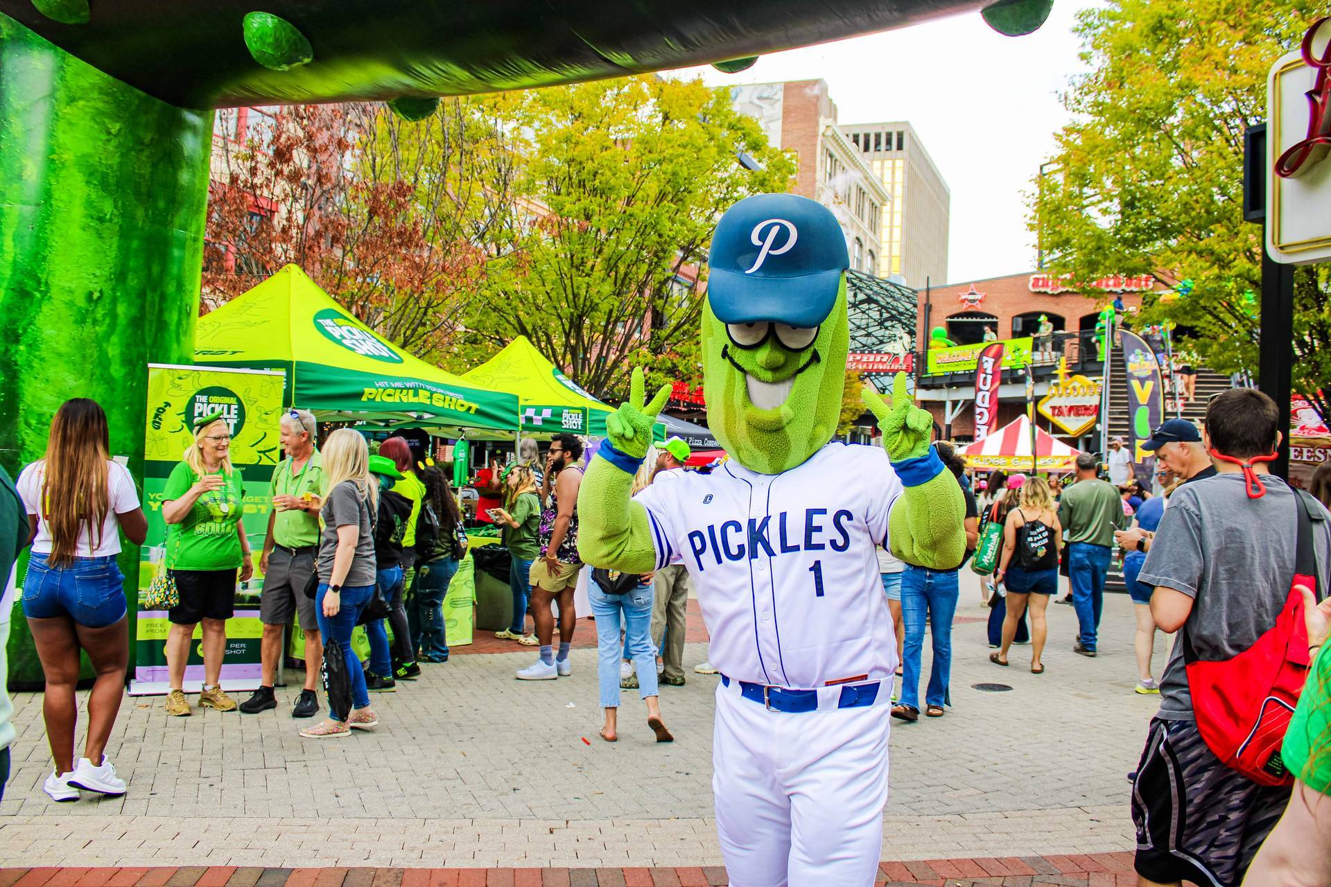 The Portland Pickles mascot poses in front of The Original Pickle Shot vendor activation under The Big Dill 30-foot inflatable pickle arch at The Big Dill pickle festival, Power Plant Live!, Baltimore Maryland 2025.
