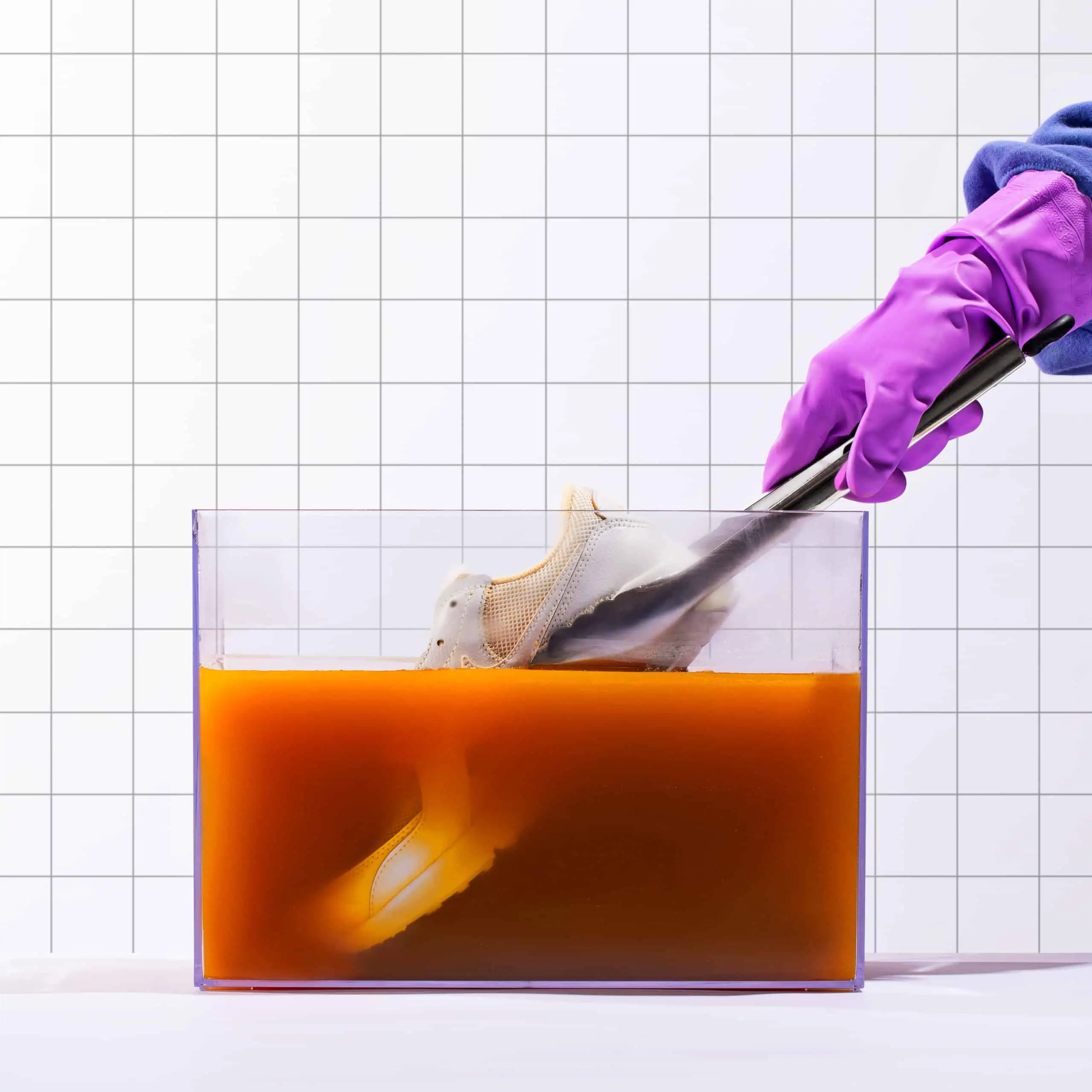 Person in gloves stirring liquid in a transparent container.