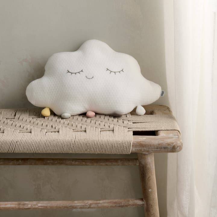 A cushion in the shape of a cloud is on top of a rattan and wood bench.