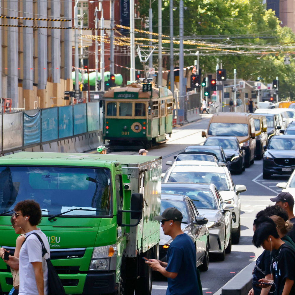 Tram on a busy street with cars and pedestrians.