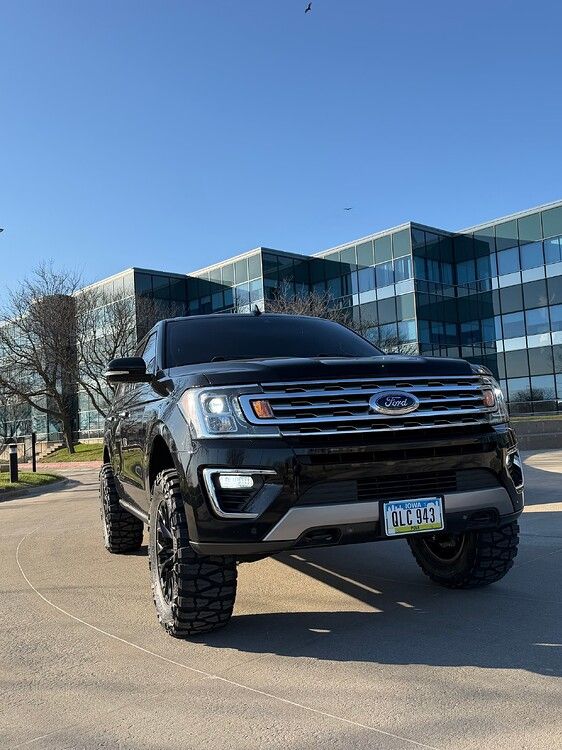 Low-angle front view Troy's lifted black 2018 Ford Expedition with headlights on before glass office building gallery photo 11