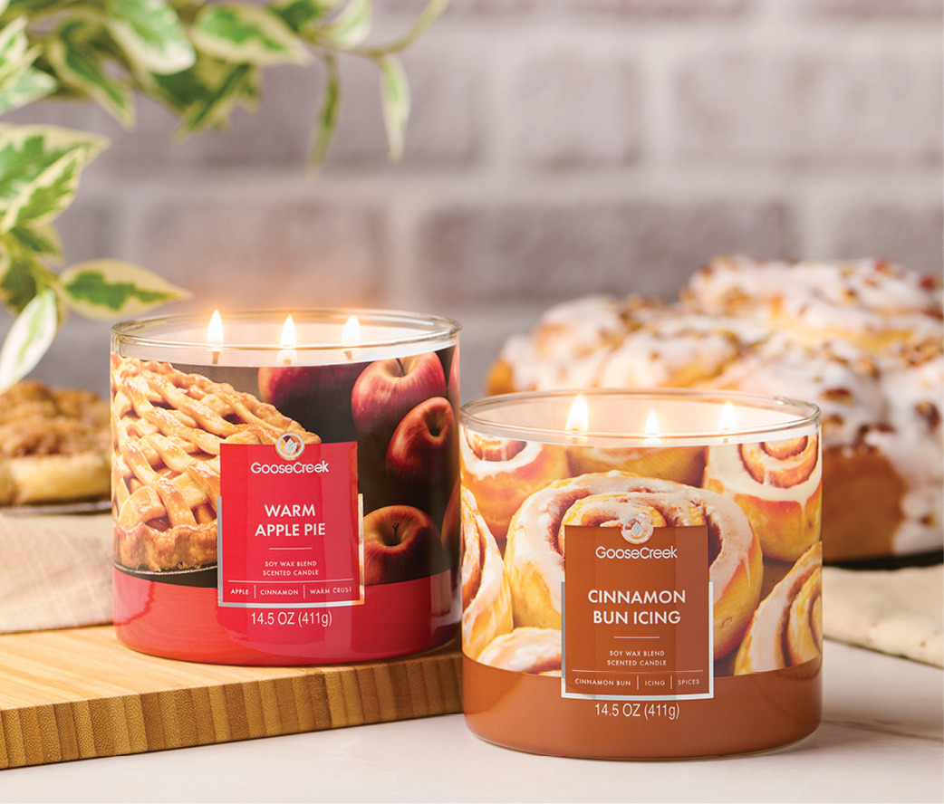 Two scented candles, apple pie and cinnamon bun, with baked goods in background.