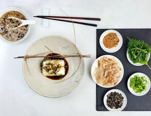 A flat lay of tofu dish with various garnishes and side dishes.