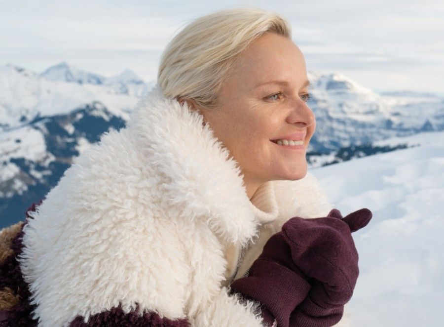 Woman smiling in winter attire against a snowy mountain backdrop.