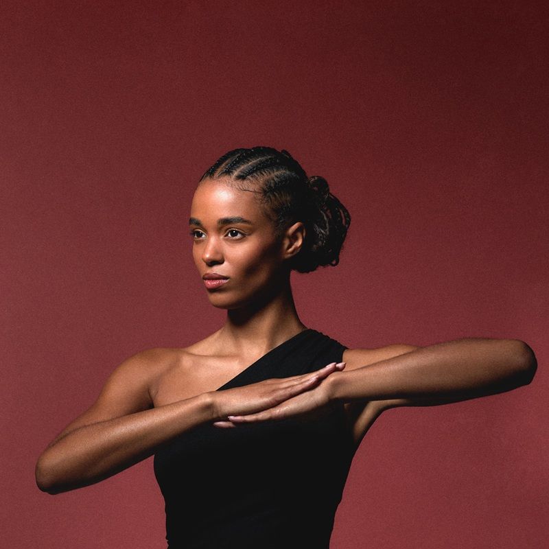 A woman in a black dress poses against a red background.