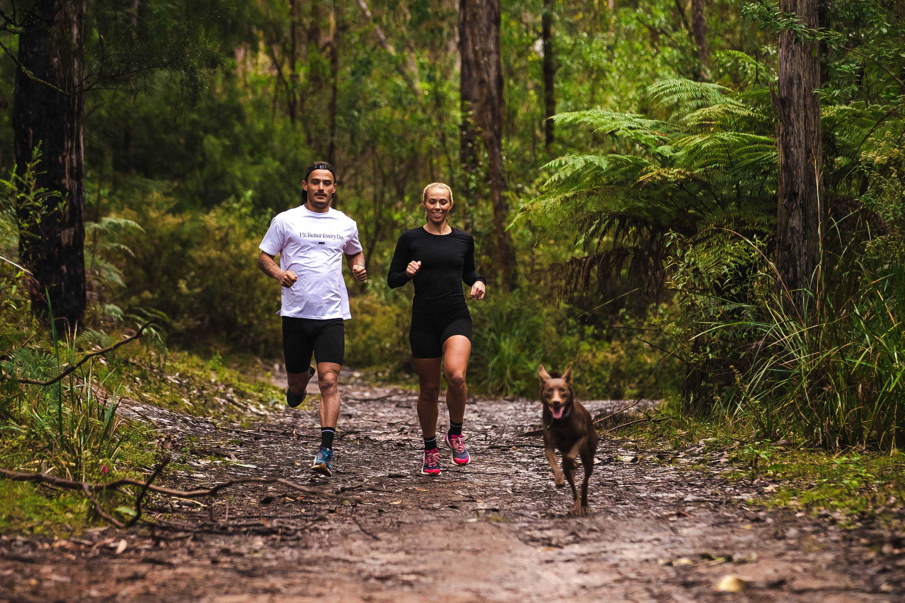 a male and female trail running with their dog 