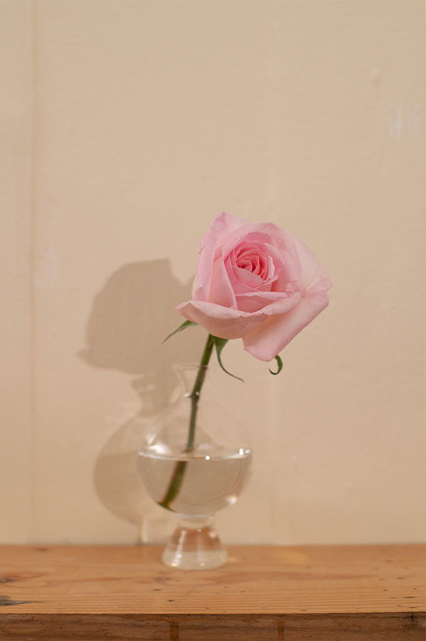 A pink rose in a clear vase on a wooden surface.
