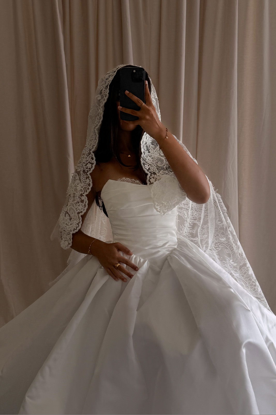 Bride wearing a white gown and veil, holding her phone in front of her face.