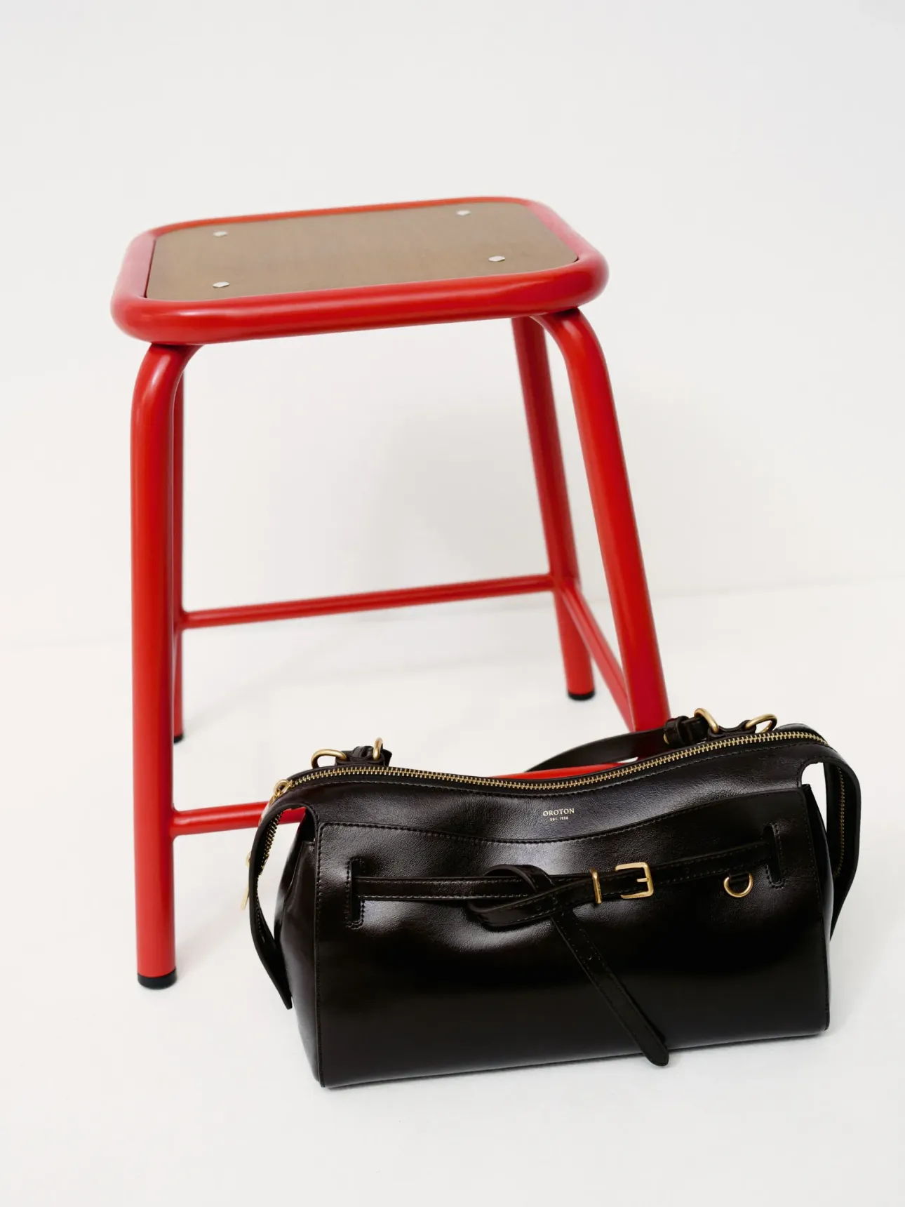 A red stool next to a black handbag on a white background.