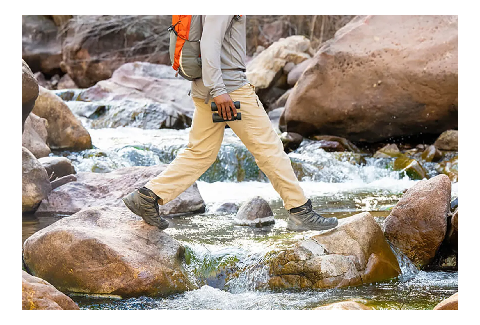 A hiker walking across a rocky stream with Nikon binoculars