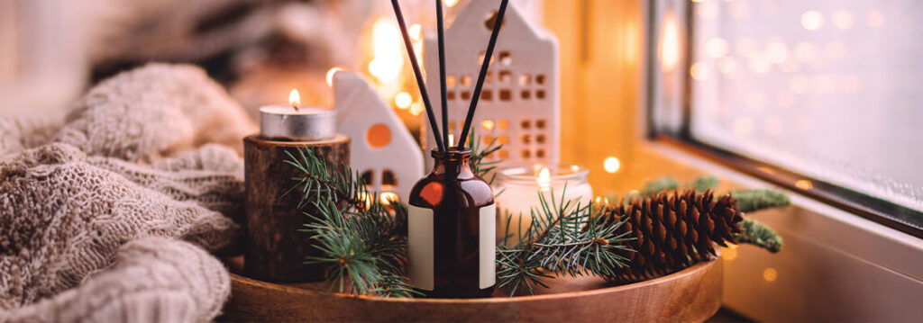 Cozy winter scene with candles, pinecones, and festive decorations by a window.