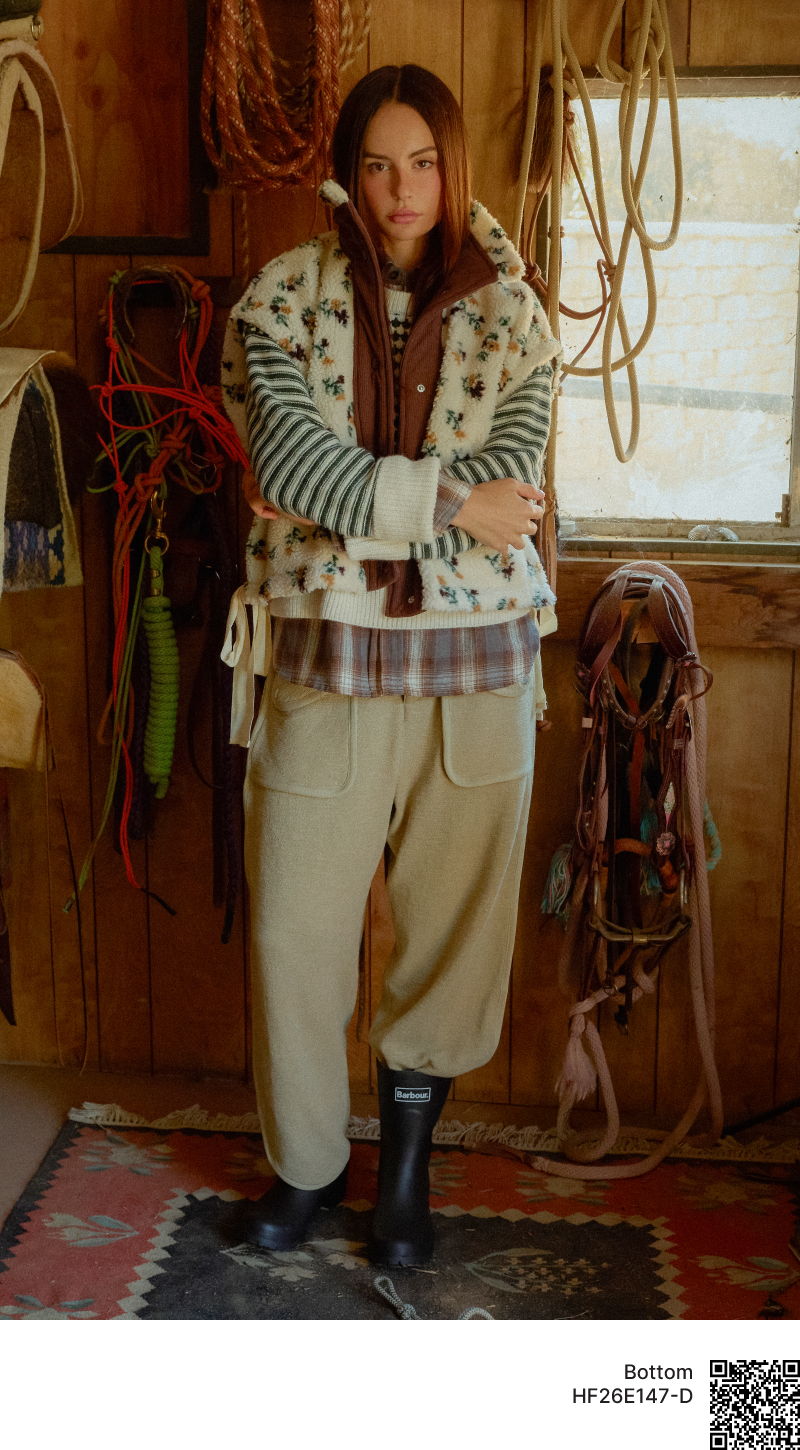 Person wearing layered clothing, standing in a rustic environment with ropes.