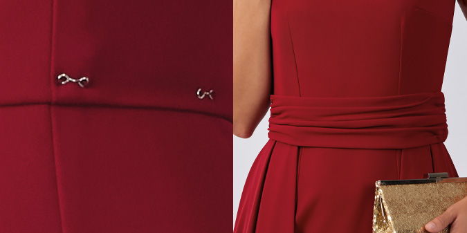 Red dress detail with a waistband and a gold clutch.