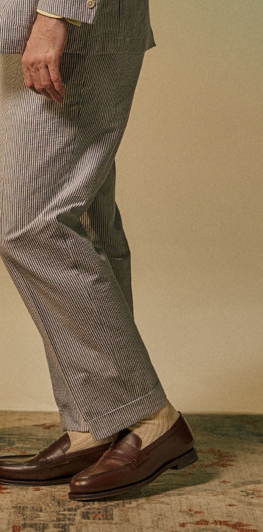 Person wearing striped pants and brown loafers, standing on a textured surface.