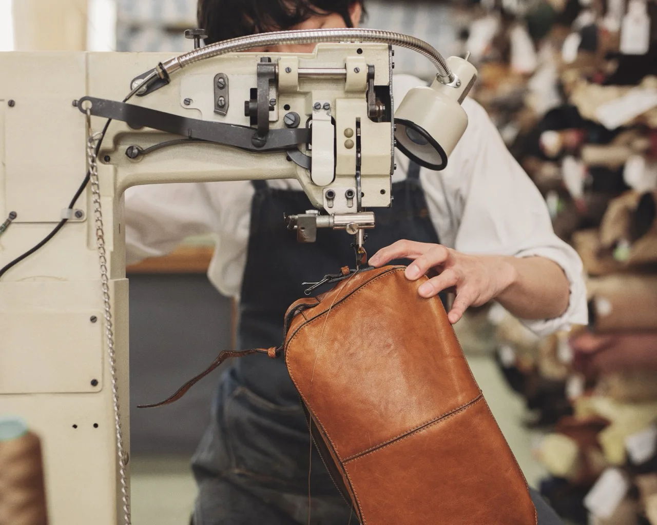 A person sewing a brown leather bag using a sewing machine.