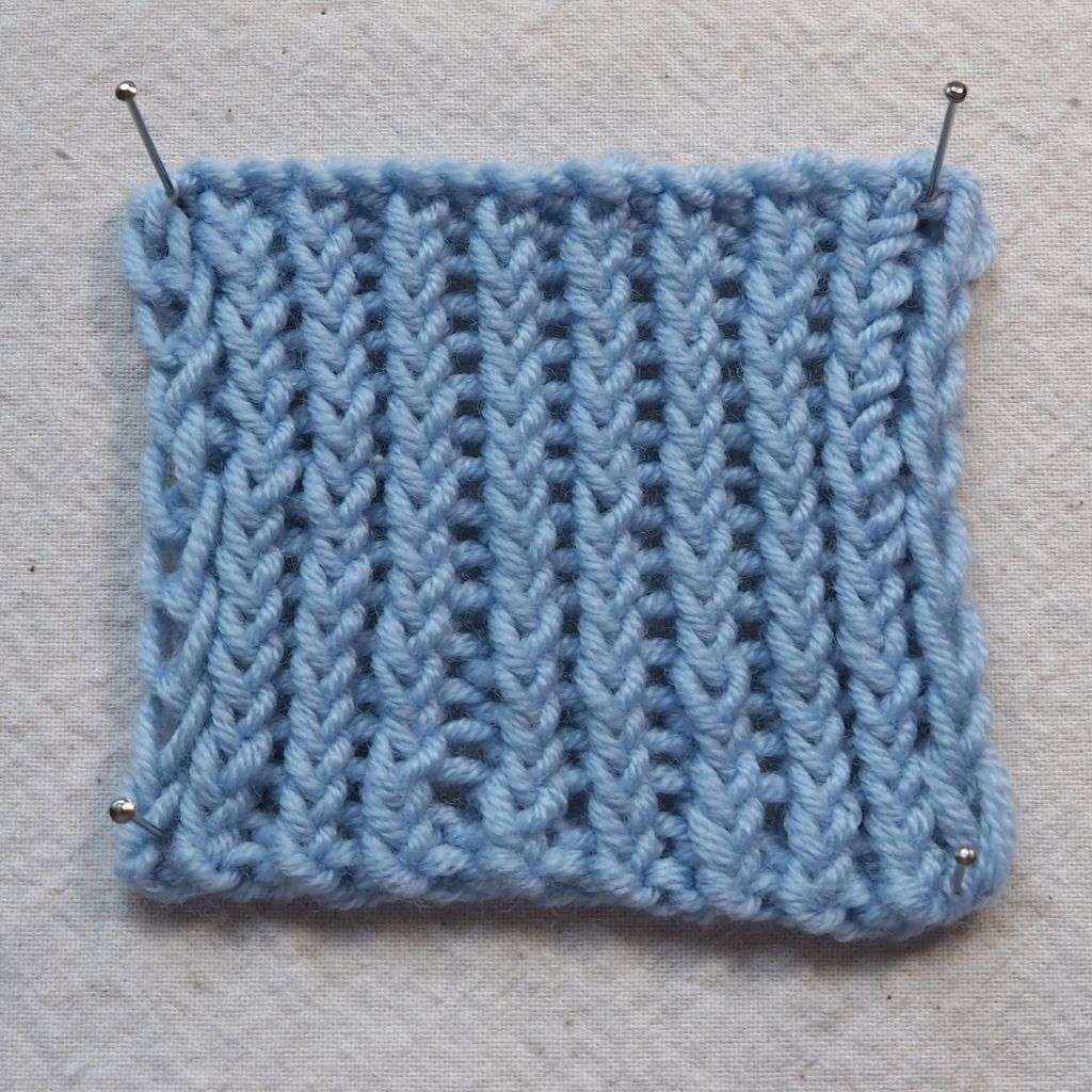 Maschenprobe aus blauem Garn die eine Maschenprobe mit verschränkten Rippen auf einer Seite zeigt.