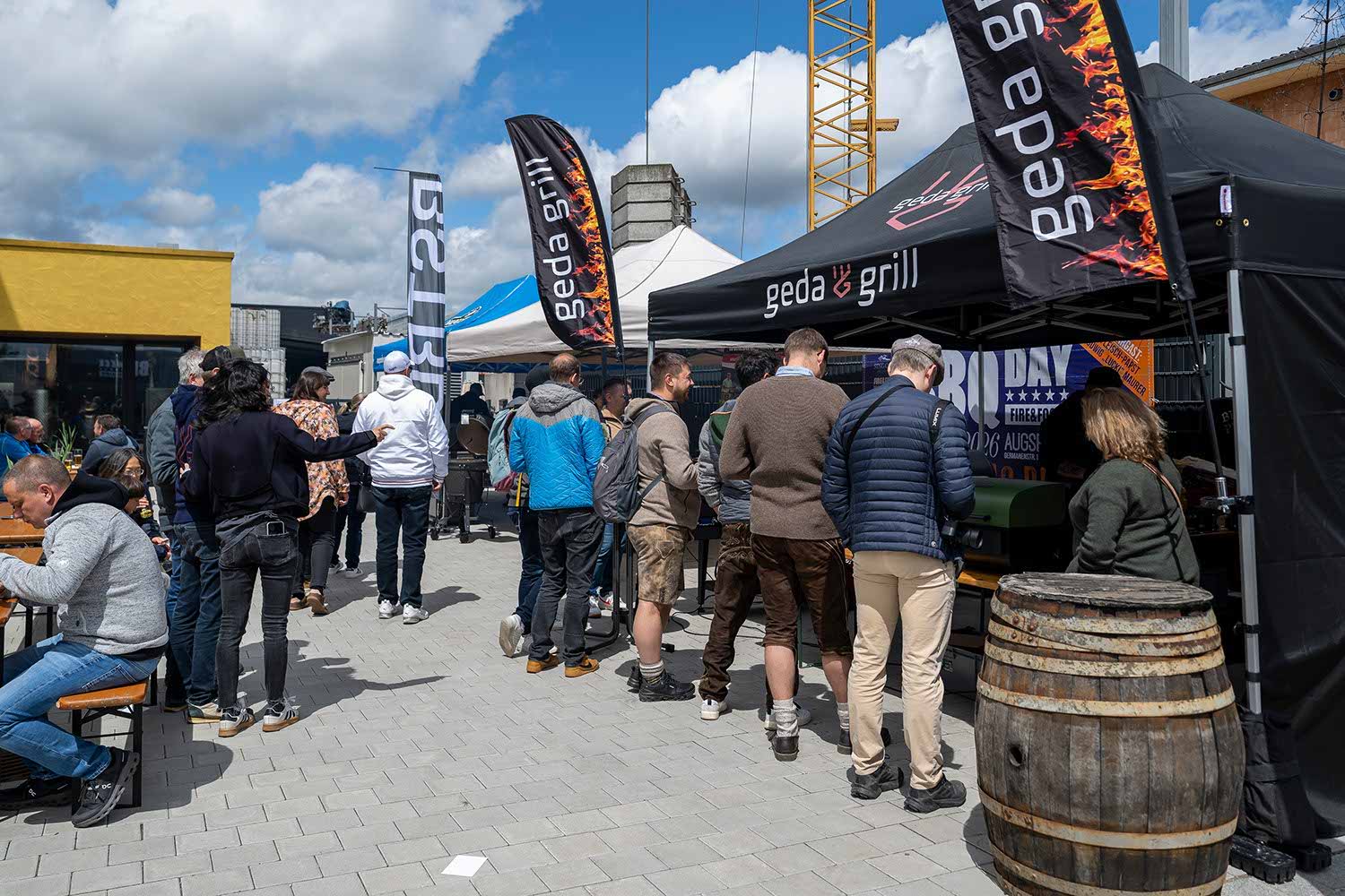 People waiting in line at an outdoor event with vendor tents.
