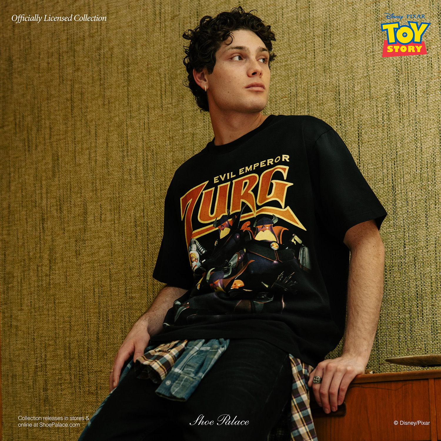 Young man in a graphic t-shirt, sitting against a textured wall.