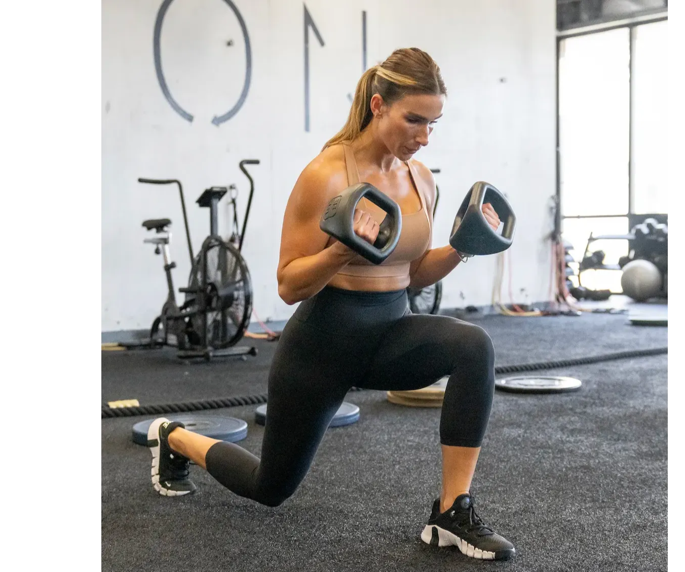 Female athlete performing a back lunge to bicep curl with YBells in center grip.