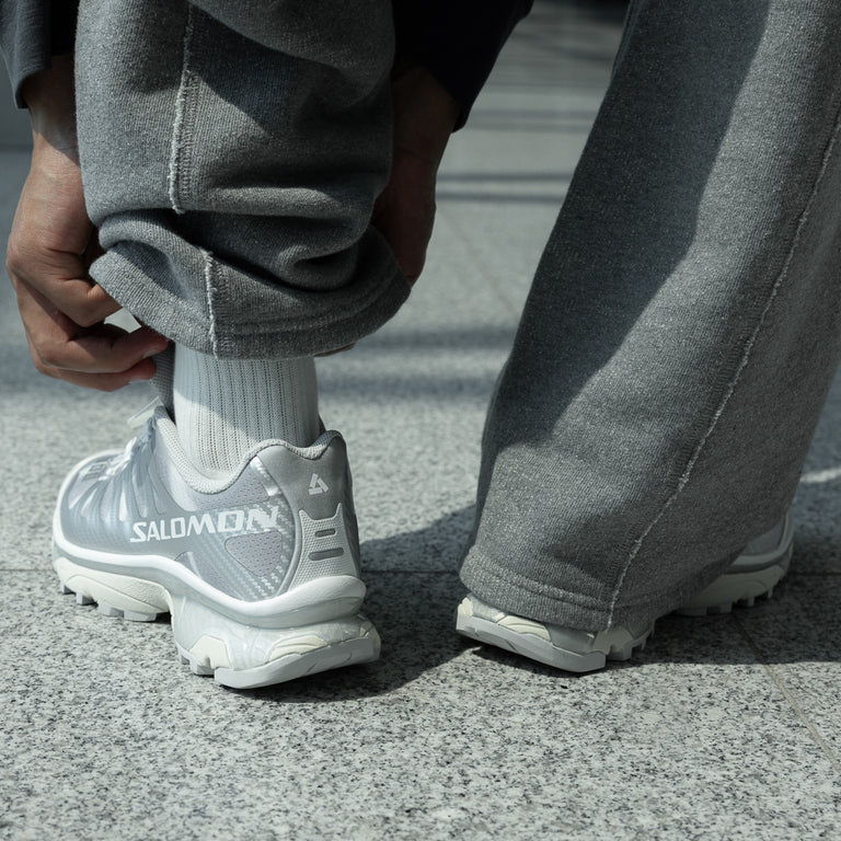 Person adjusting gray sweatpants and sporting silver athletic shoes.