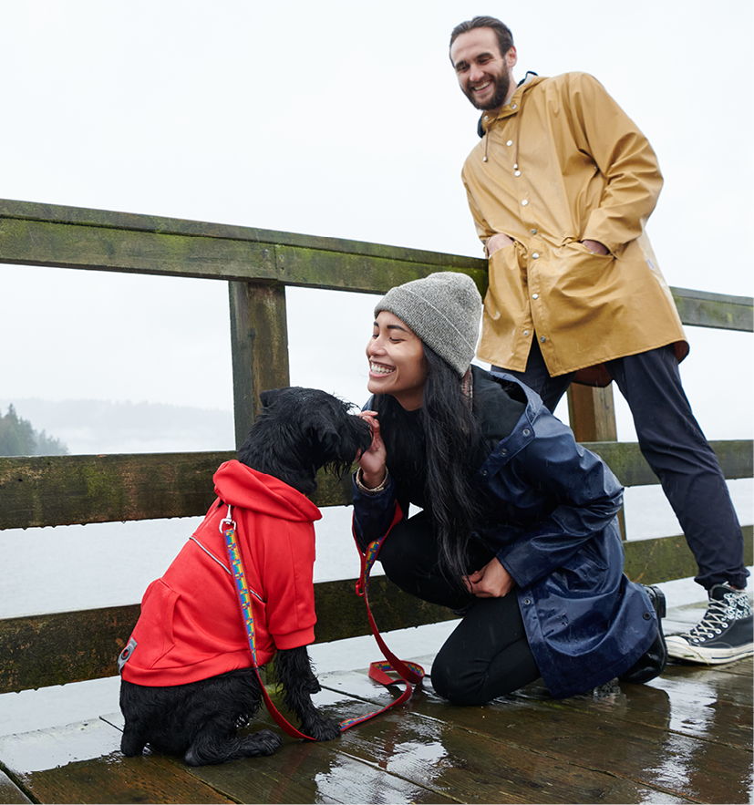 A woman and a dog on a rainy bridge, with a man in the background.