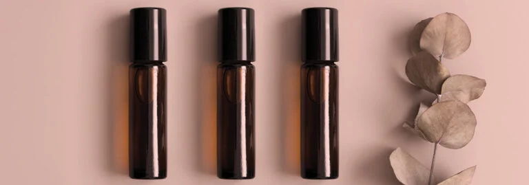 Three amber glass bottles on a pink background with dried leaves.