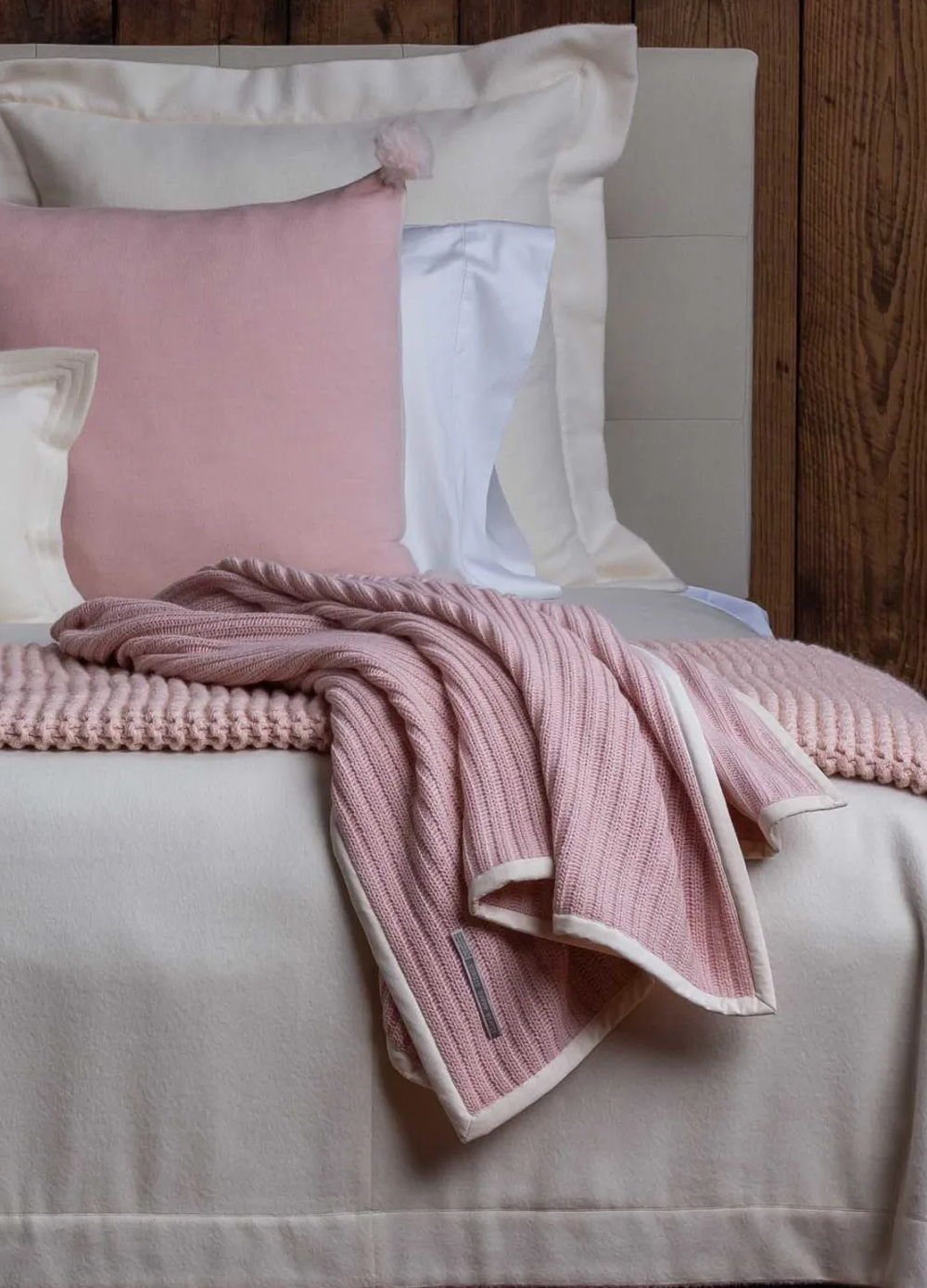 Cozy bed with pink and cream pillows and a textured blanket.
